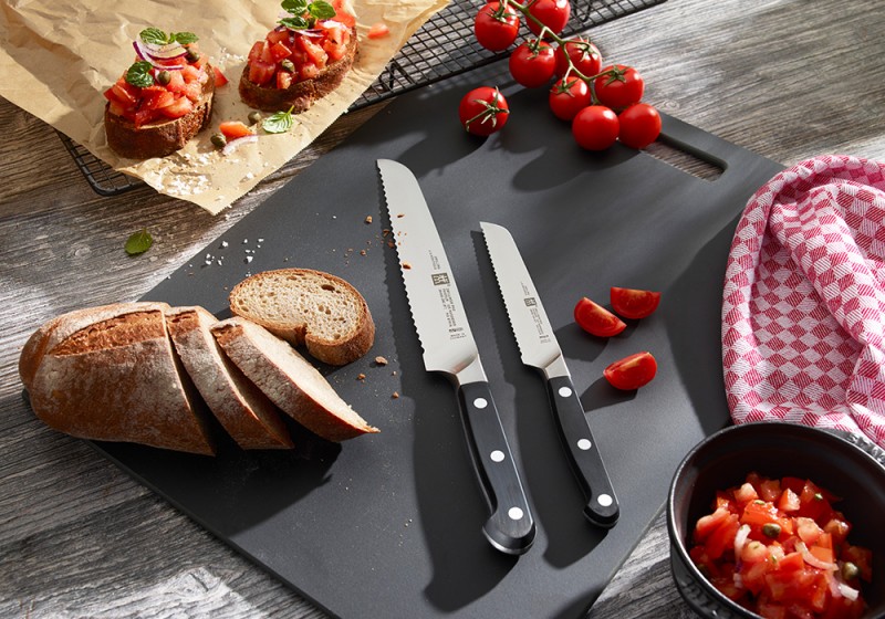 Zwei Brotmesser liegen auf einem Brettchen, zusammen mit Brot